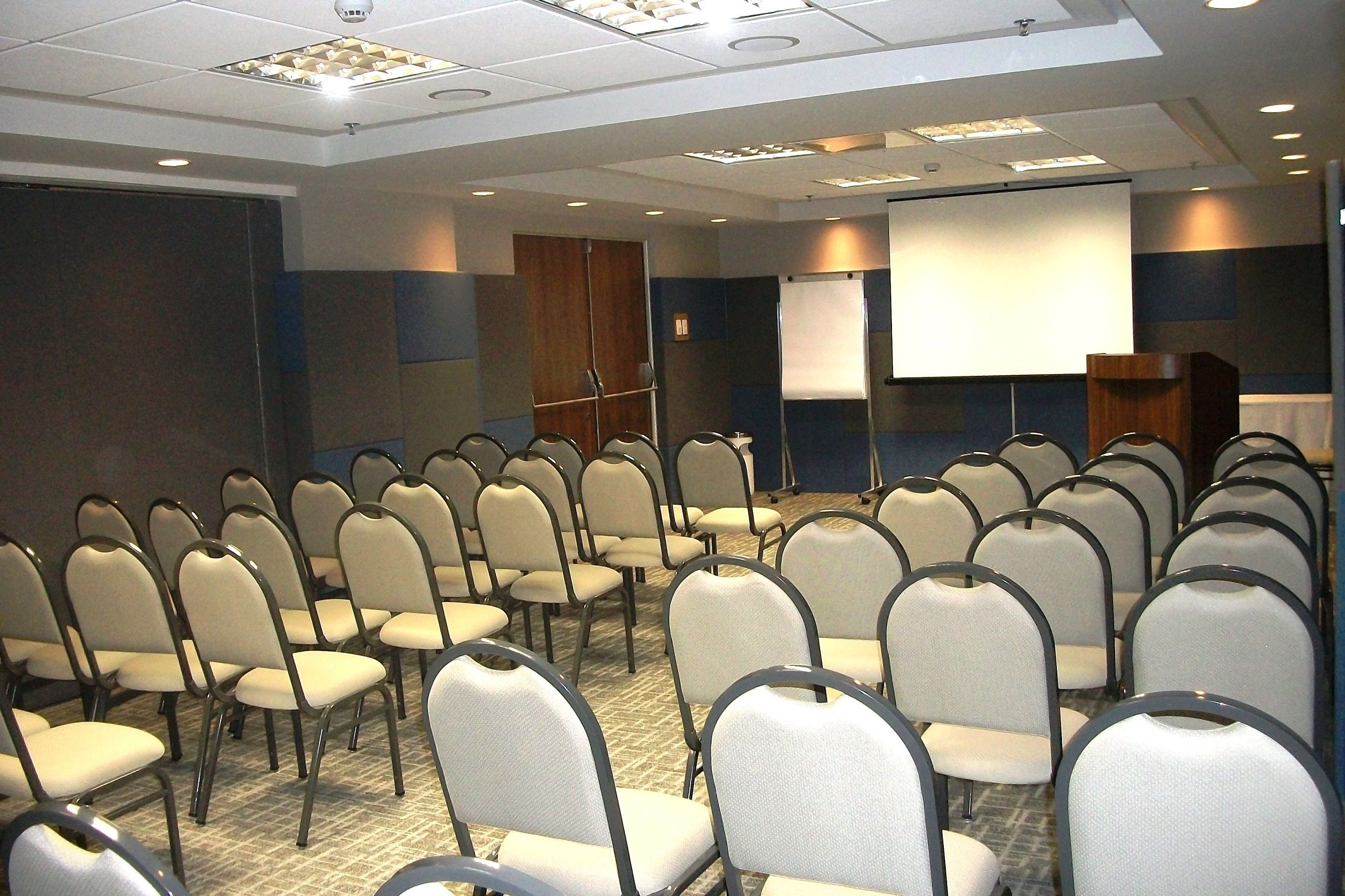 A conference room with rows of chairs, a podium, a projection screen, and a whiteboard.