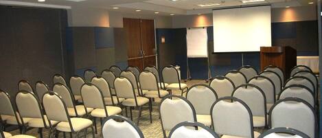 A conference room with rows of chairs, a podium, a projection screen, and a whiteboard.