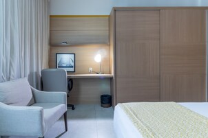 A hotel room with a bed, a desk with a computer, a chair, a lamp, and a wardrobe.