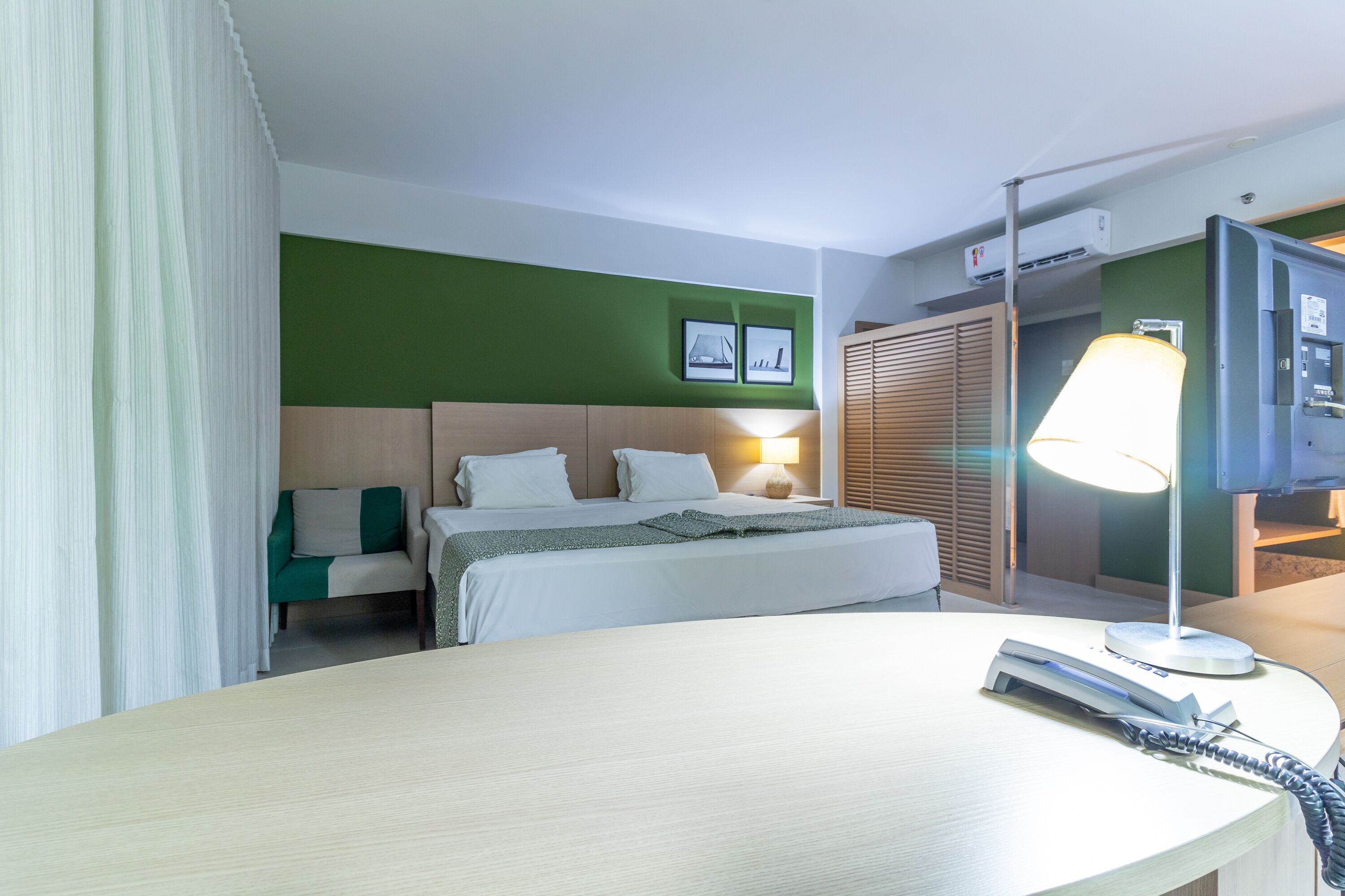 Ein Hotelzimmer mit Bett, Schreibtisch, Lampe, Fernseher und Kleiderschrank.