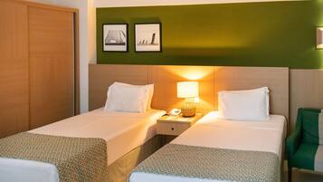 A hotel room with two beds, a nightstand with a lamp, a green chair, and two framed pictures on the wall.