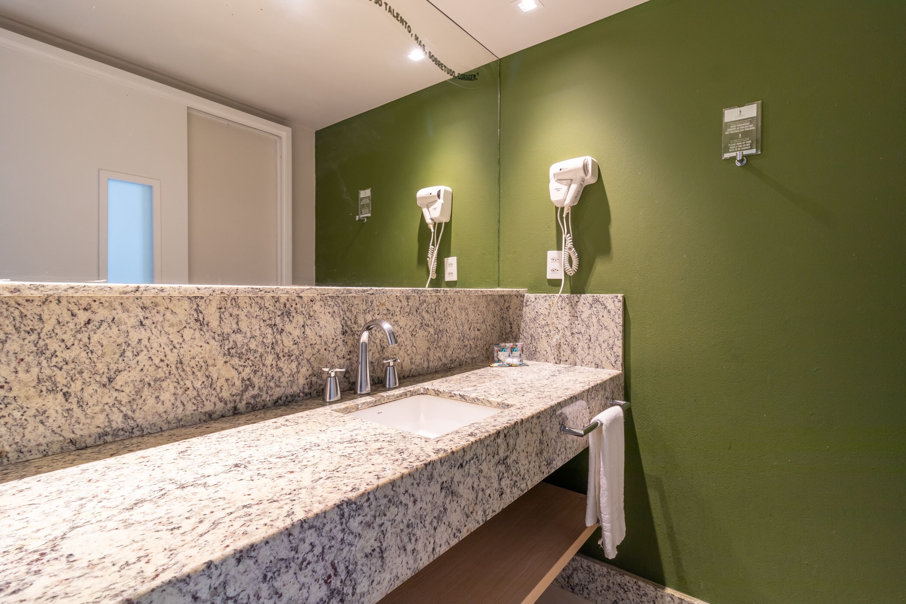 A bathroom with a granite countertop, two sinks, a mirror, and a green wall.