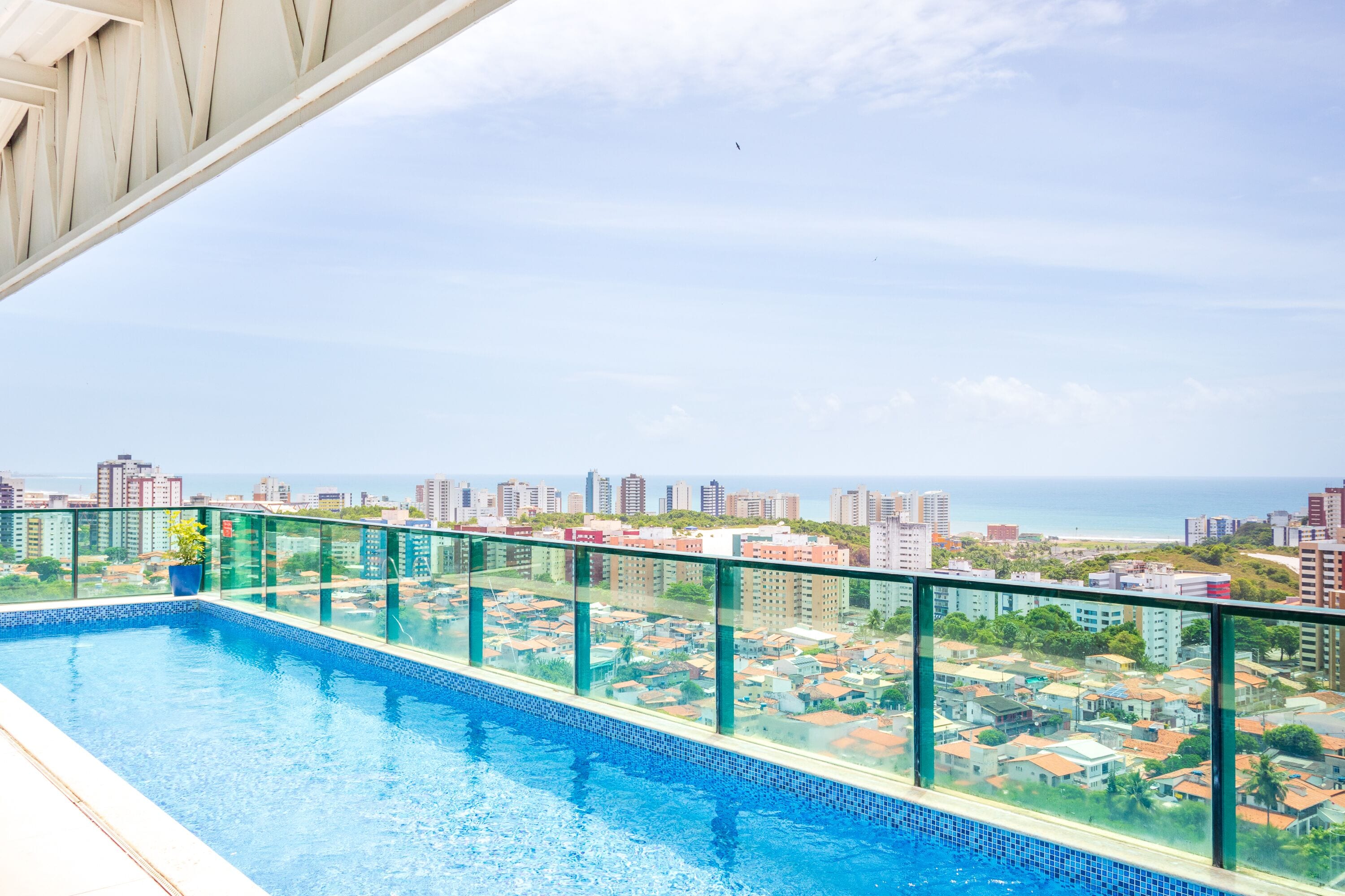 Piscina no terraço com guarda-corpo de vidro, com vista para a cidade e praia.