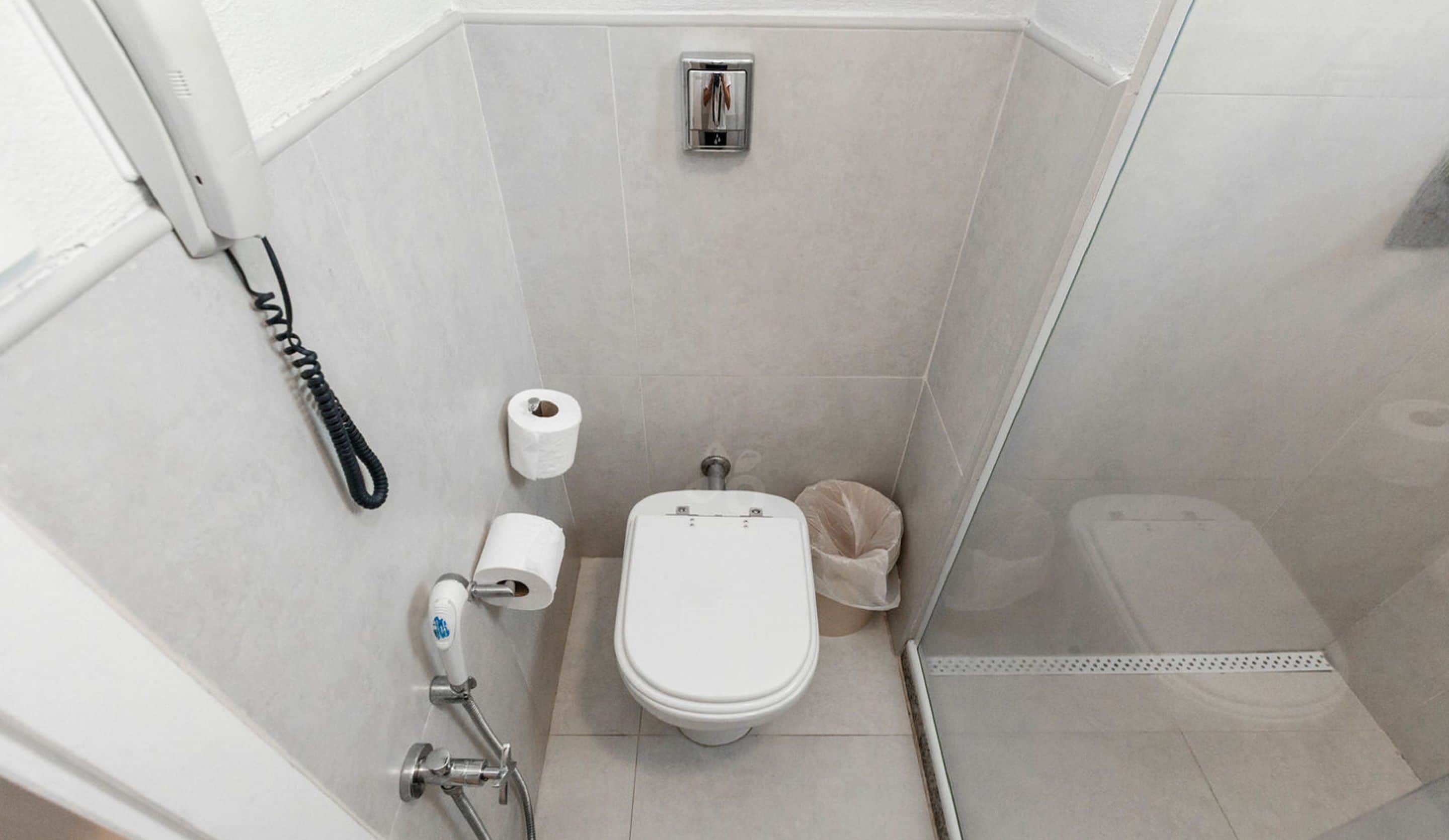 Un baño pequeño y moderno con inodoro, ducha y soporte para papel higiénico.