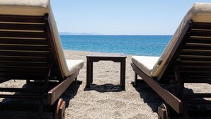 Two wooden lounge chairs with cushions facing a pebble beach and the sea. - Thirides Beach Resort (East Mani)