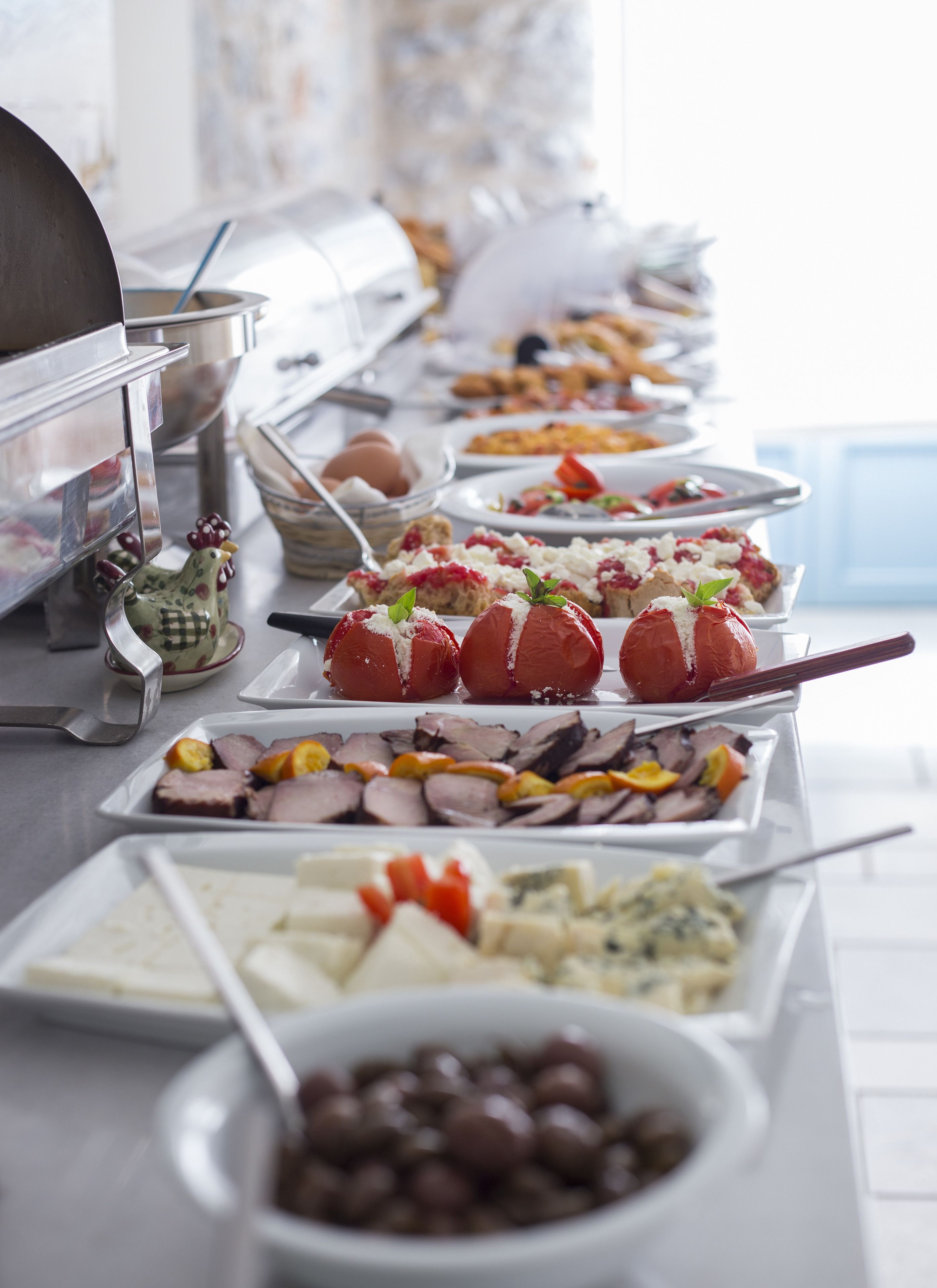 A buffet with various dishes including stuffed tomatoes, meats, cheeses, and olives.
