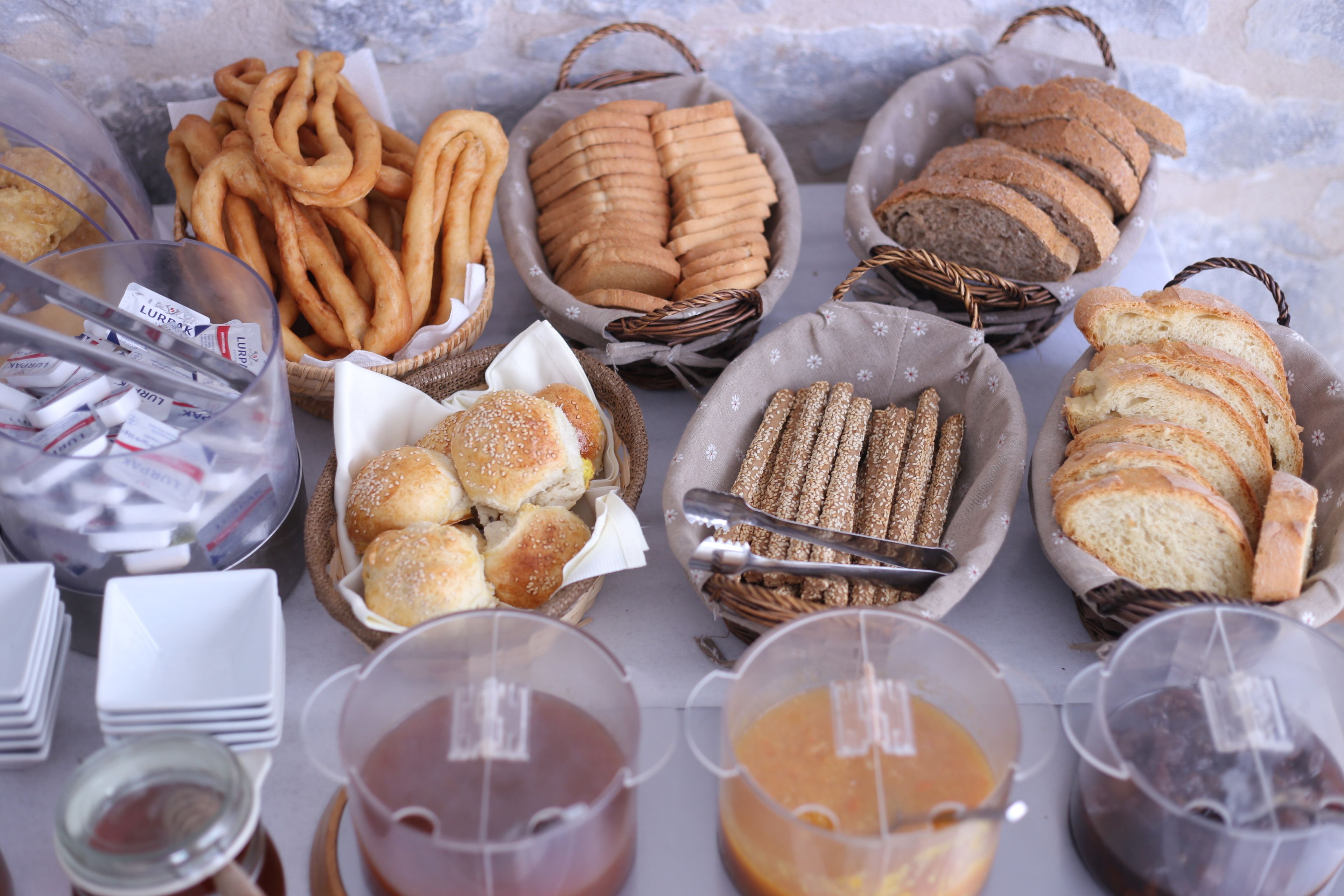 A variety of baked goods including pretzels, bread rolls, and sliced bread, along with several containers of sauces.
