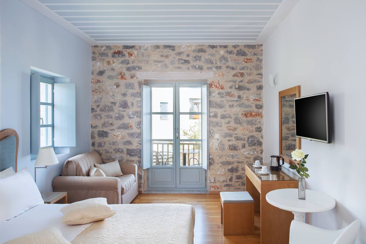 A bedroom with a stone wall, a bed, a sofa, a TV, and a balcony.