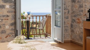A room with a wooden floor, a stone wall, a table with chairs, and a view of the sea through an open door. - Thirides Beach Resort (East Mani)