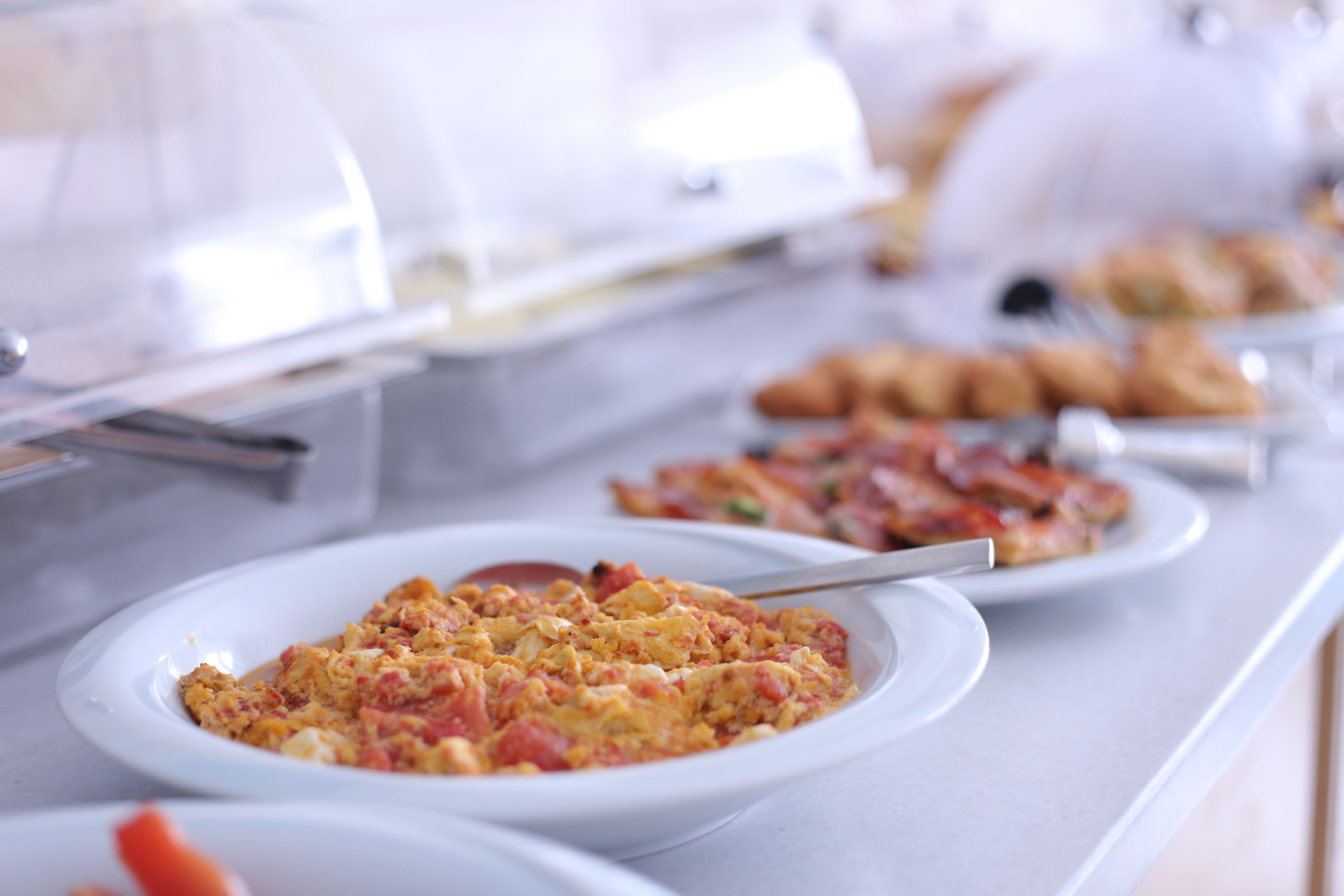 Un bufé con diversos platos, incluyendo huevos revueltos, tocino y productos de pastelería.