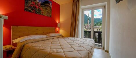Une chambre d’hôtel avec un grand lit, une table de chevet, un tableau au mur et un balcon offrant une vue sur la ville.