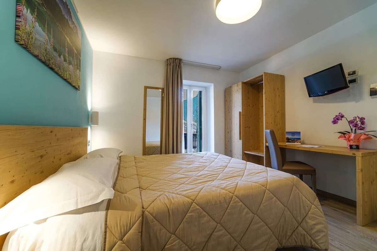 Een hotelkamer met een groot bed, een bureau met een computer, een televisie en een raam met gordijnen.