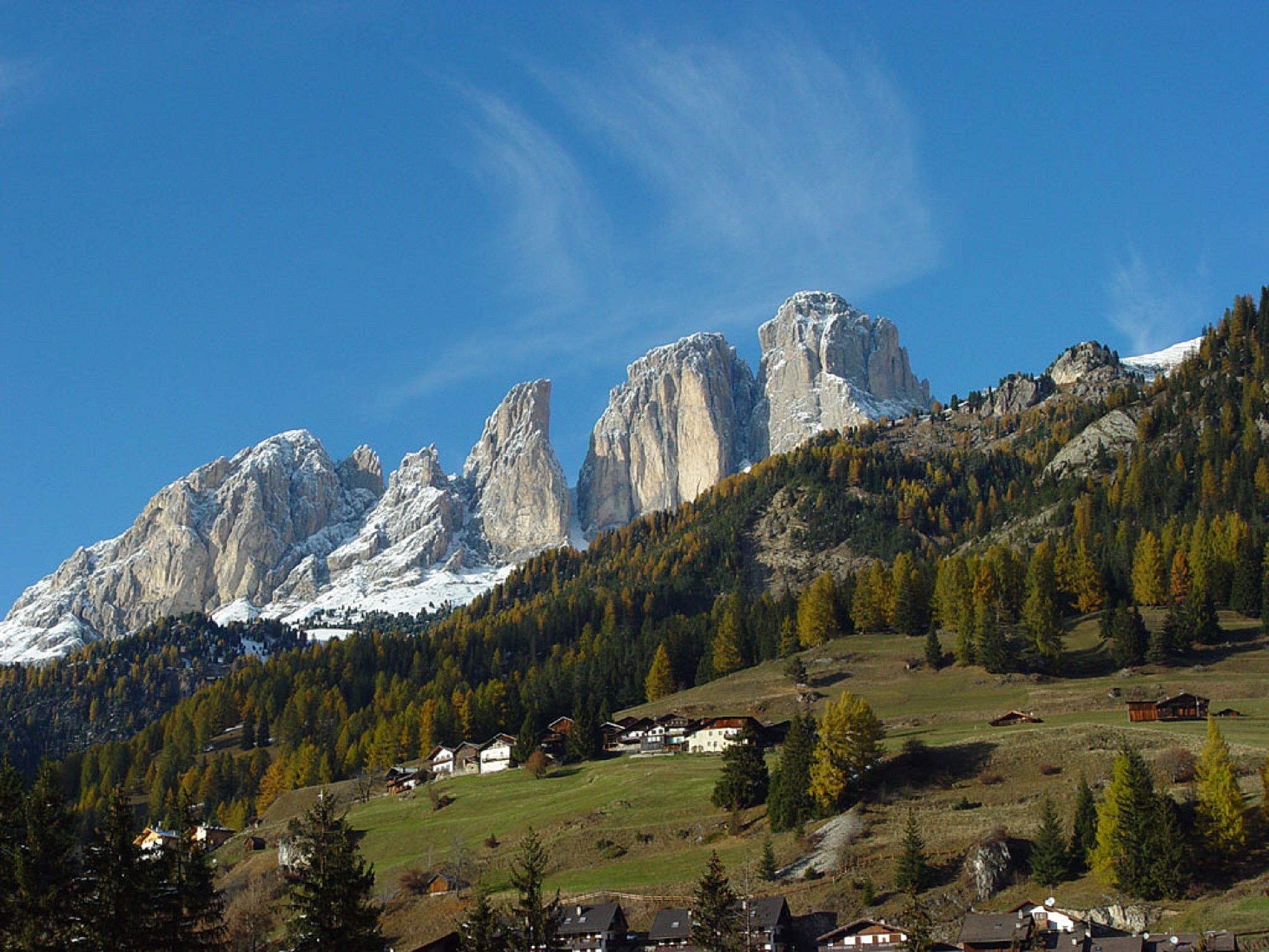 Un paisaje montañoso con picos rocosos, una zona boscosa y casas dispersas.