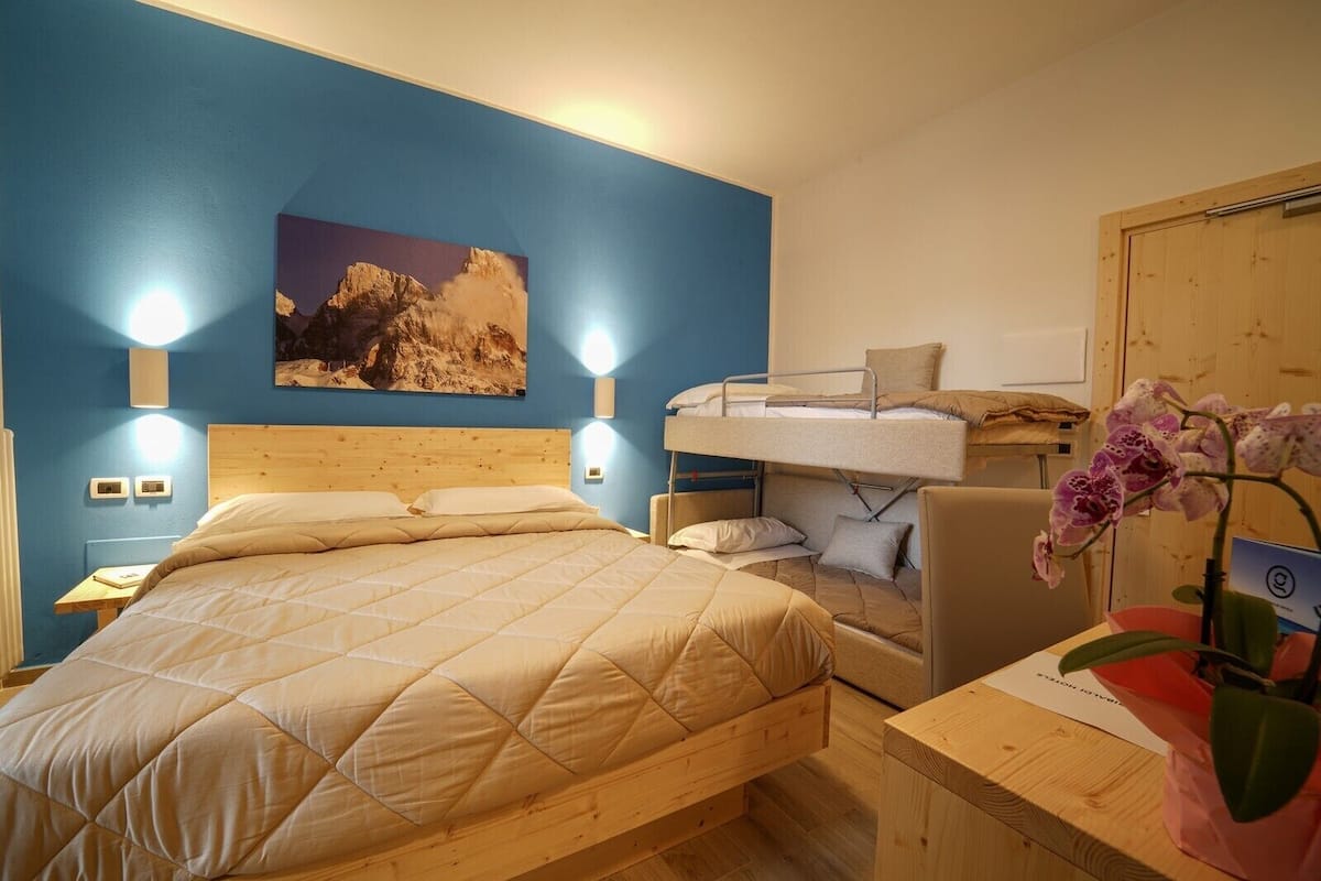 Een slaapkamer met een stapelbed, een enkel bed, een houten hoofdbord, een nachtkastje, een wandlamp, een schilderij en een potorkidee.