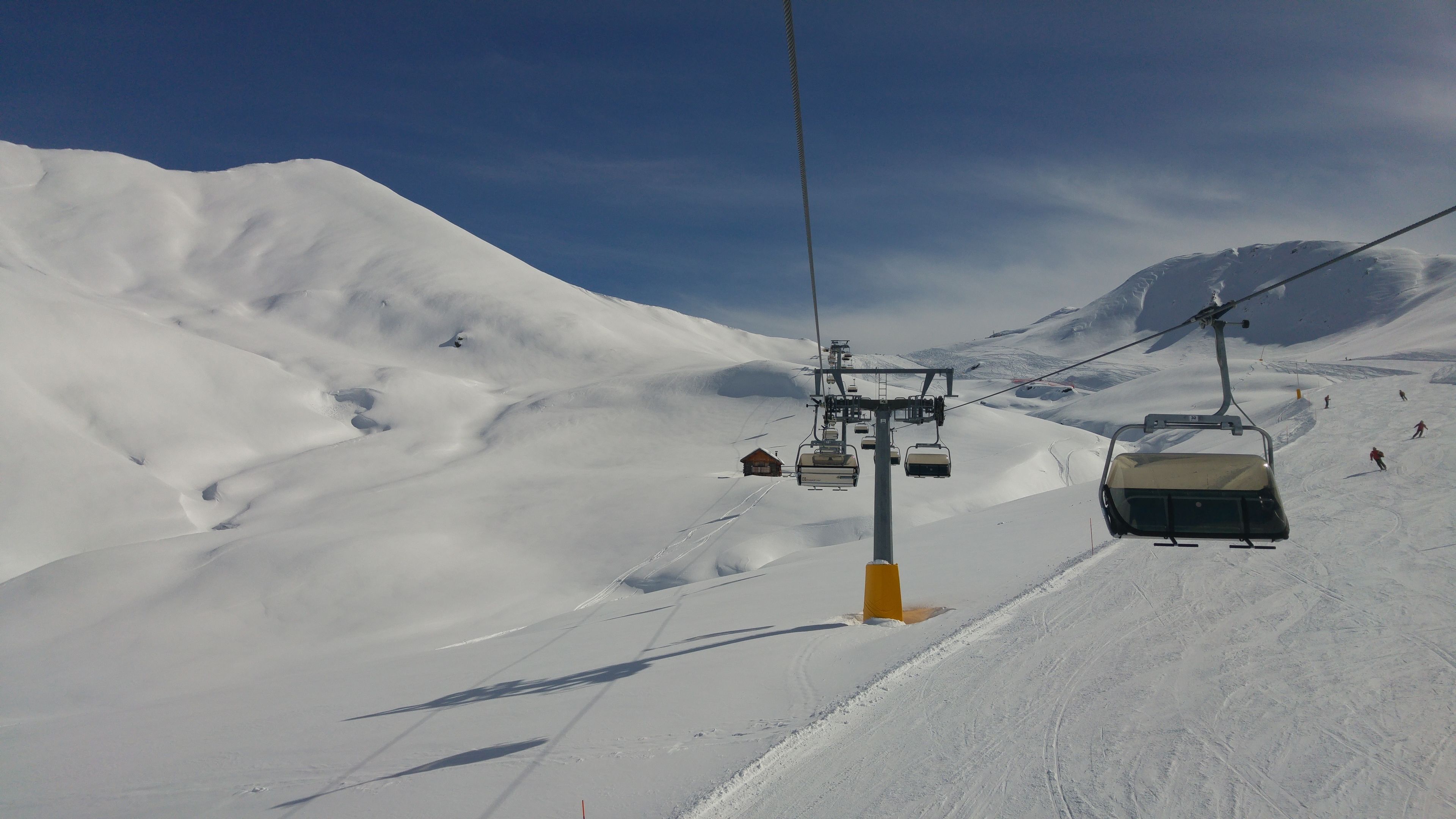 Un asiento de telesilla subiendo una pendiente nevada bajo un cielo despejado.