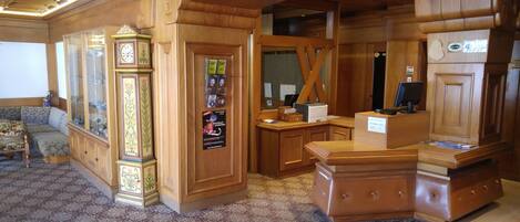 A wooden interior with a reception desk, a large clock, and a seating area.