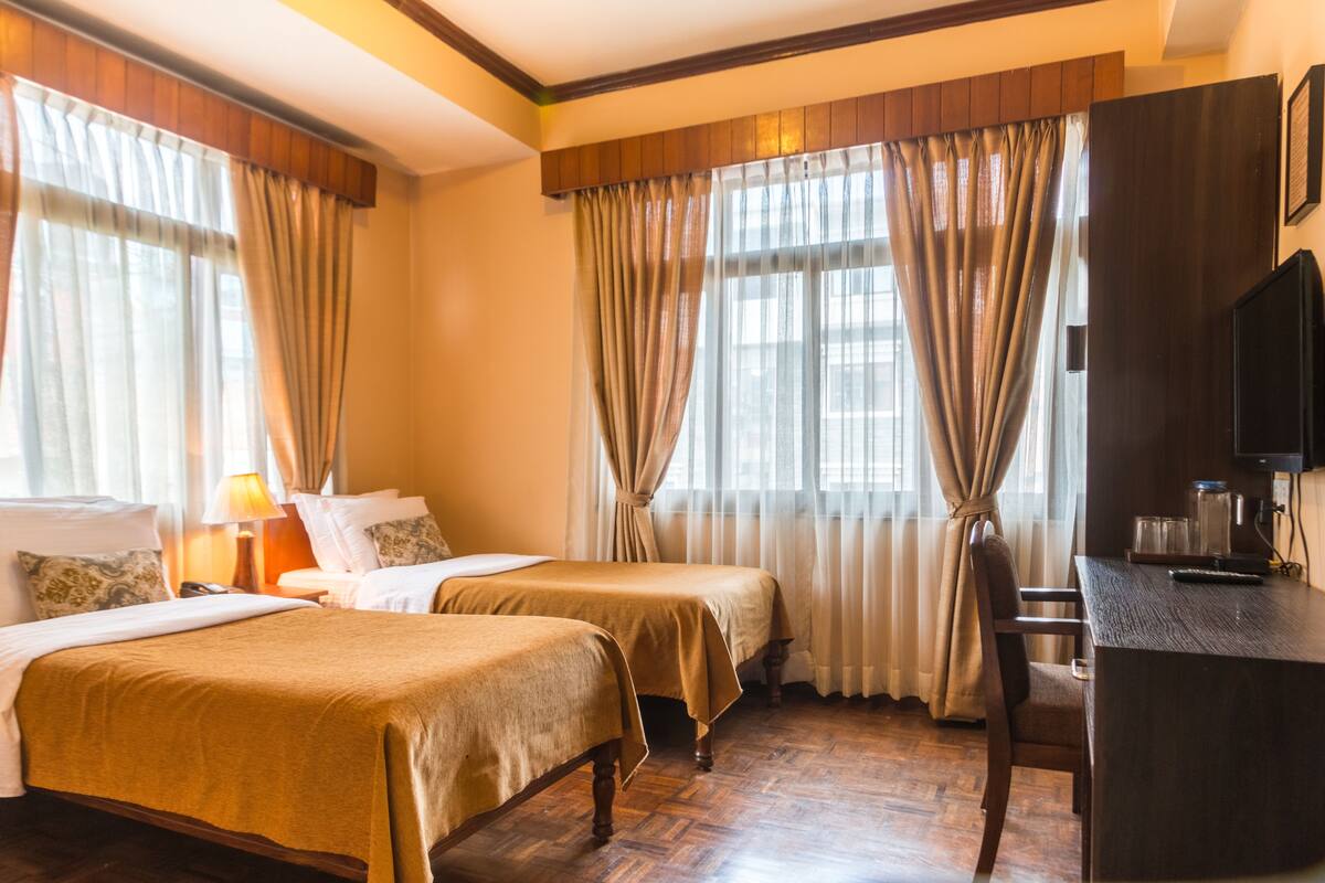 A hotel room with two beds, a desk, and a television.