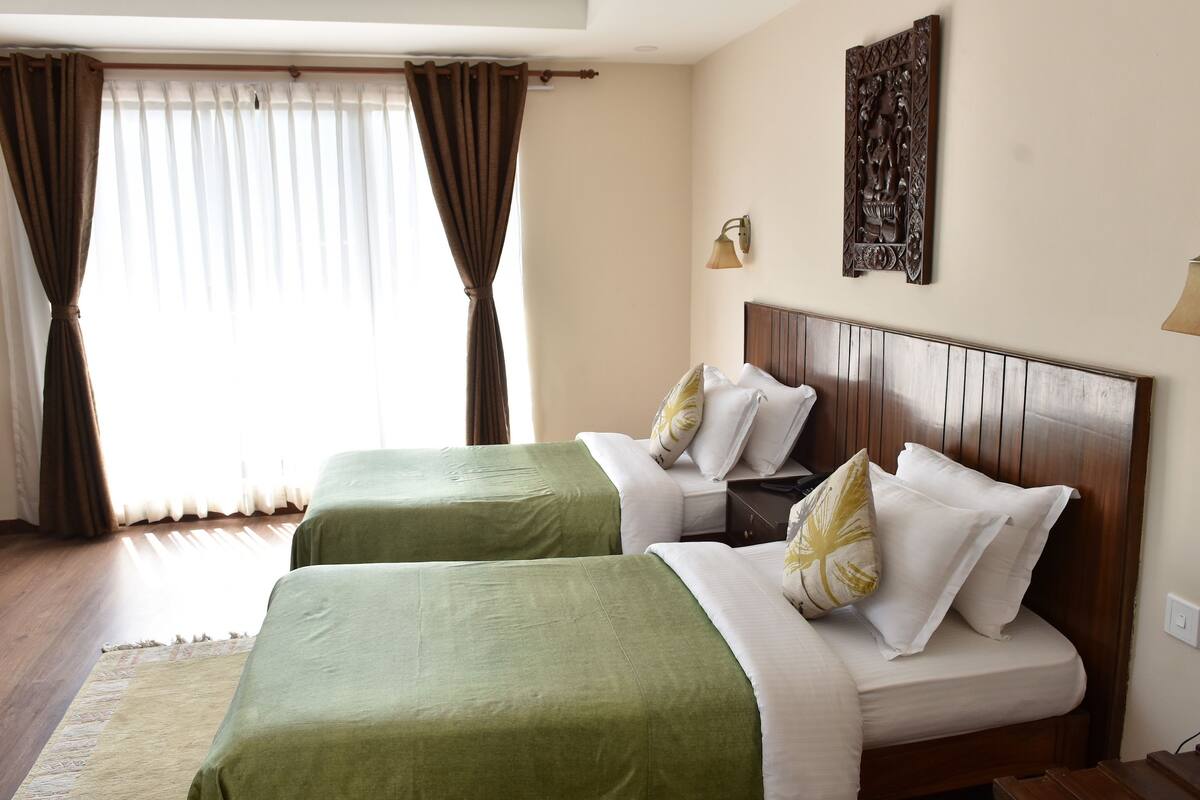 A hotel room with two beds, a wooden headboard, a wall-mounted lamp, and a decorative piece above the bed.