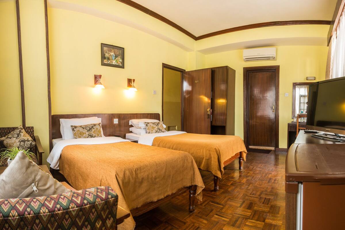 A hotel room with two beds, a TV, a desk, and a chair.