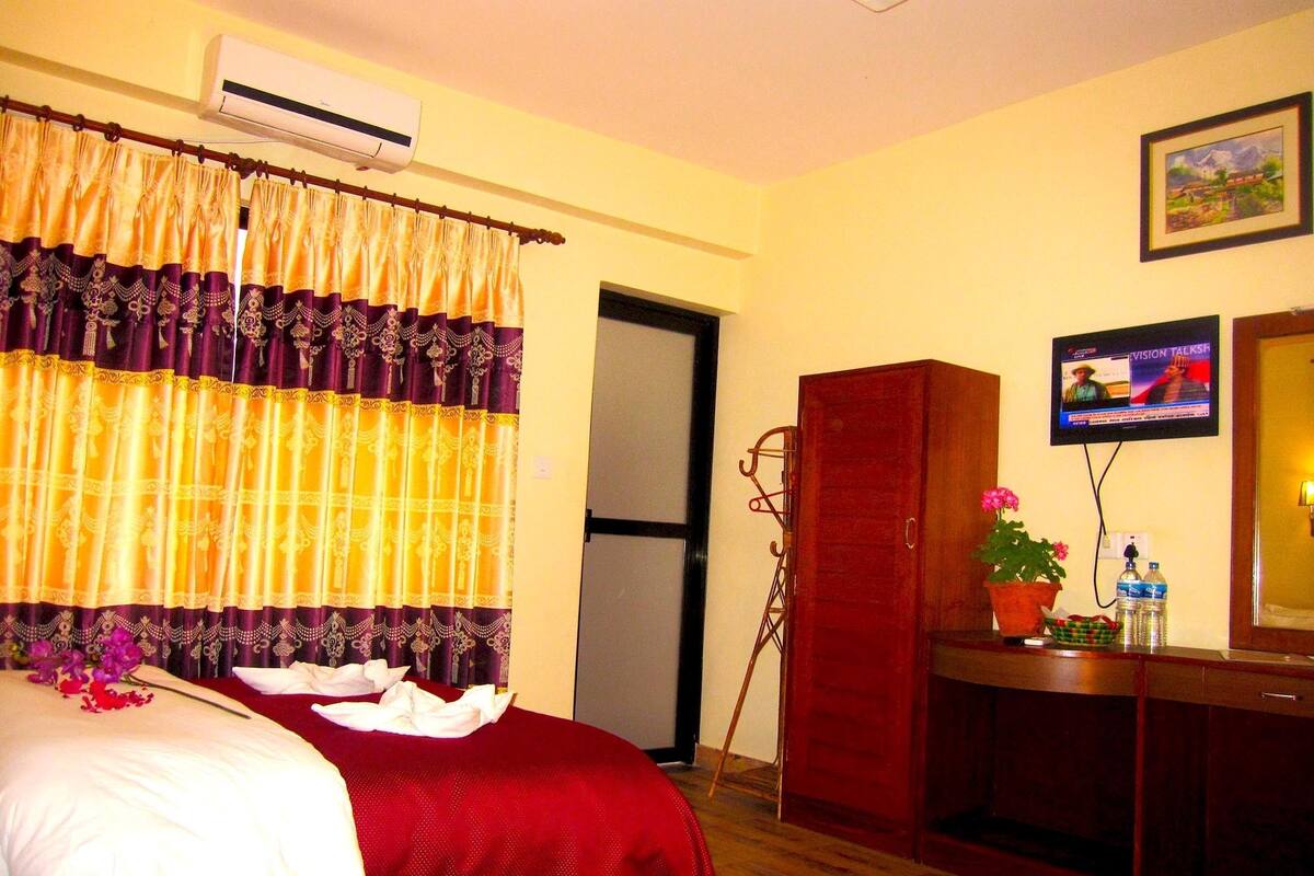 A hotel room with a bed, a wooden wardrobe, a television, and a potted plant.