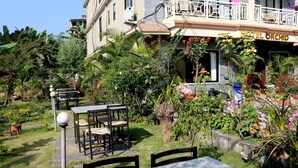 A hotel with a garden patio featuring tables and chairs, surrounded by lush greenery and flowering plants. - Hotel Orchid (Pokhara)