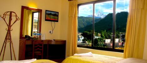 A hotel room with two beds, a desk, a chair, a mirror, and a window with a mountain view.