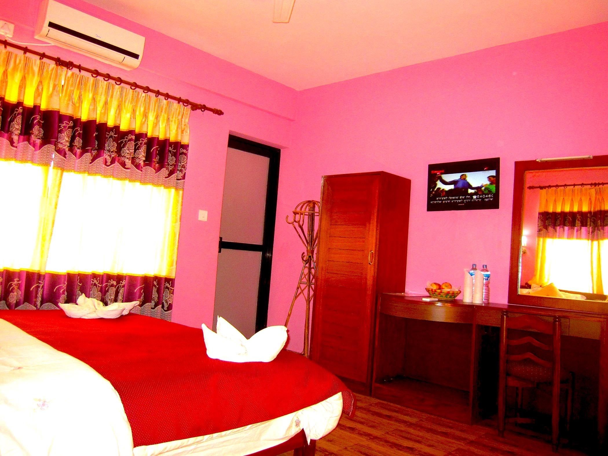 A hotel room with a bed, a desk, a chair, an air conditioner, a television, and a mirror.