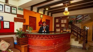 A reception desk with a red brick design, a wooden staircase, and framed certificates on the wall. - Hotel Orchid (Pokhara)