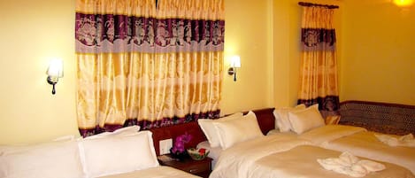 Habitación de hotel con tres camas, cada una con ropa blanca y toallas. Hay lámparas de pared y un equipo de aire acondicionado sobre las camas.