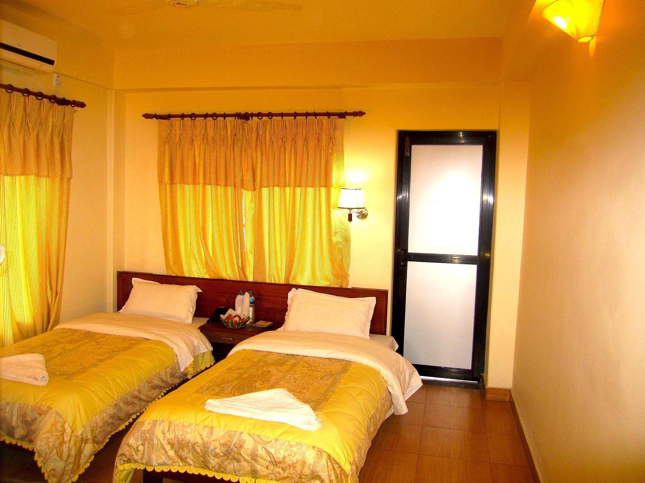 Una habitación de hotel con dos camas, una mesita de noche, una lámpara y una puerta.