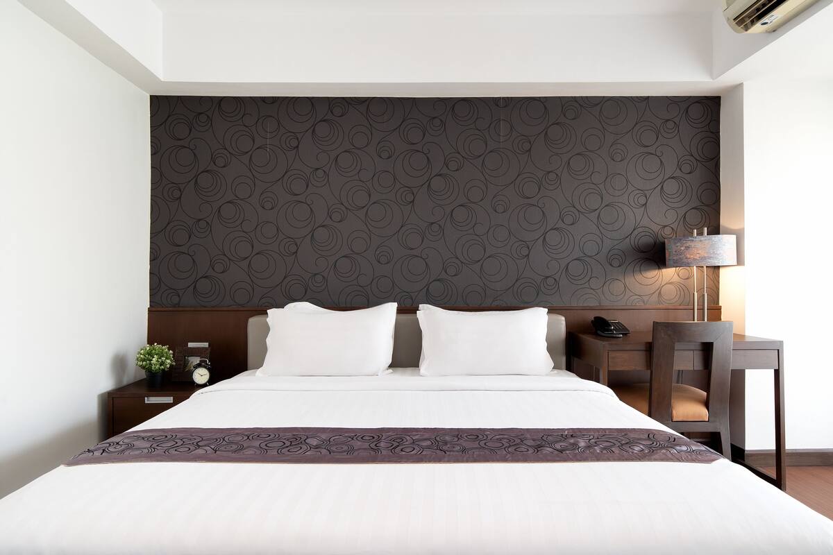Hotellihuone, jossa on suuri sänky, työpöytä tuolilla, yöpöytä lampun kanssa ja seinä, jossa on pyöreä kuvio.
