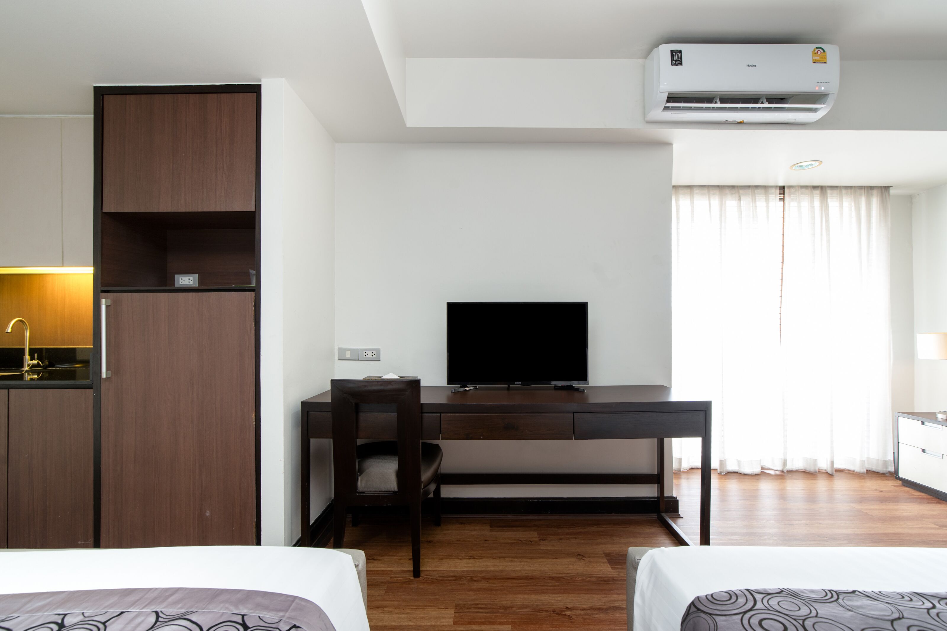 A hotel room with a bed, a desk with a TV, a wardrobe, and an air conditioner.
