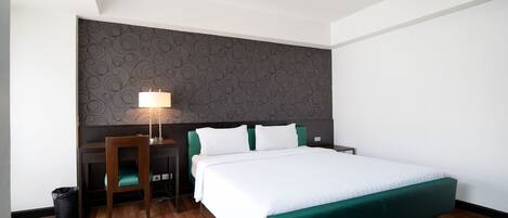 A hotel room with a bed, a desk, a chair, a lamp, and a patterned wall.