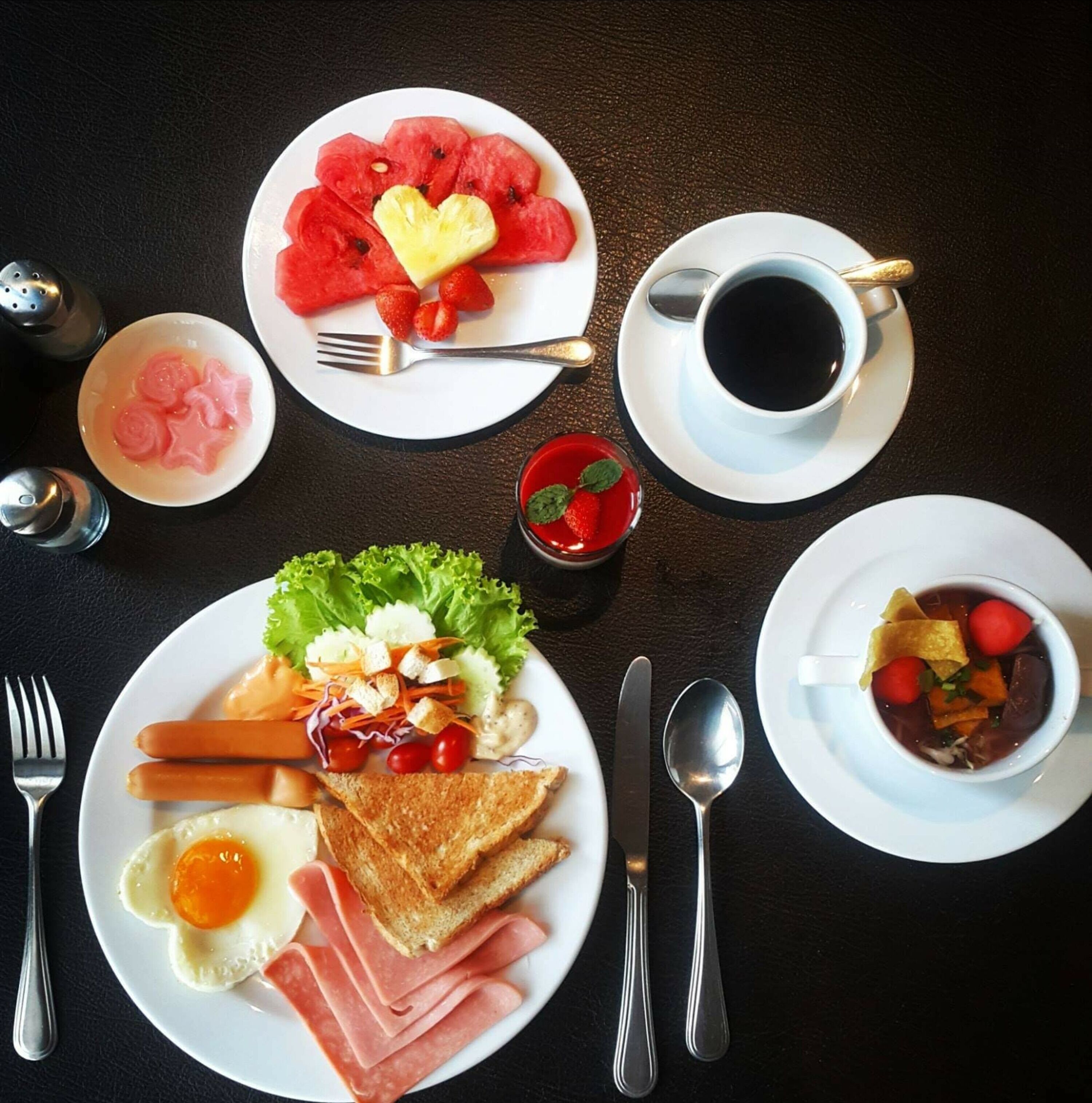 Ein Frühstückstisch mit Toast, Eiern, Schinken, Gemüse, einer Tasse Kaffee und einer Schüssel Suppe.