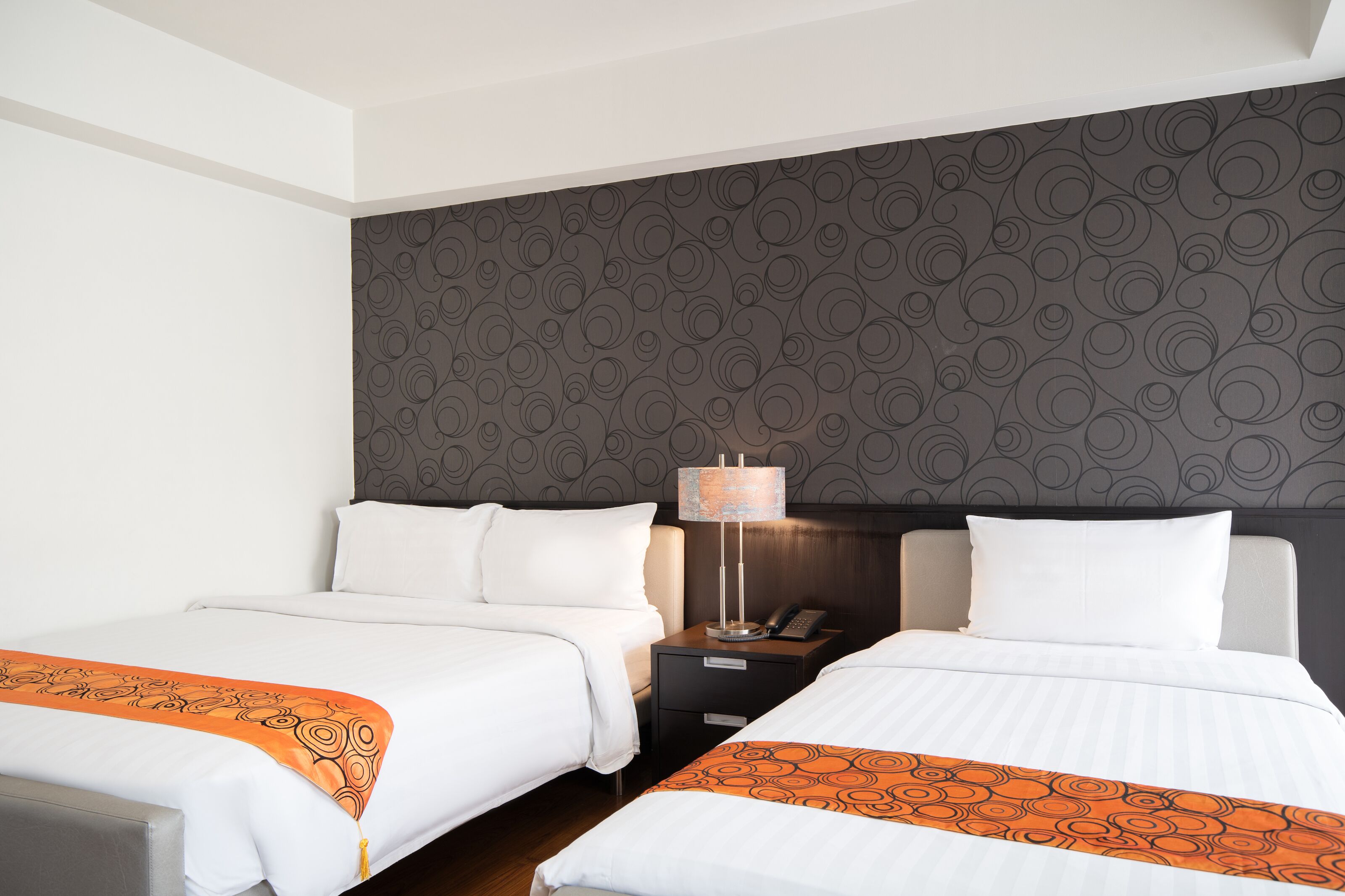 Une chambre d’hôtel avec deux lits, une table de chevet avec une lampe et un mur décoré d’un motif.
