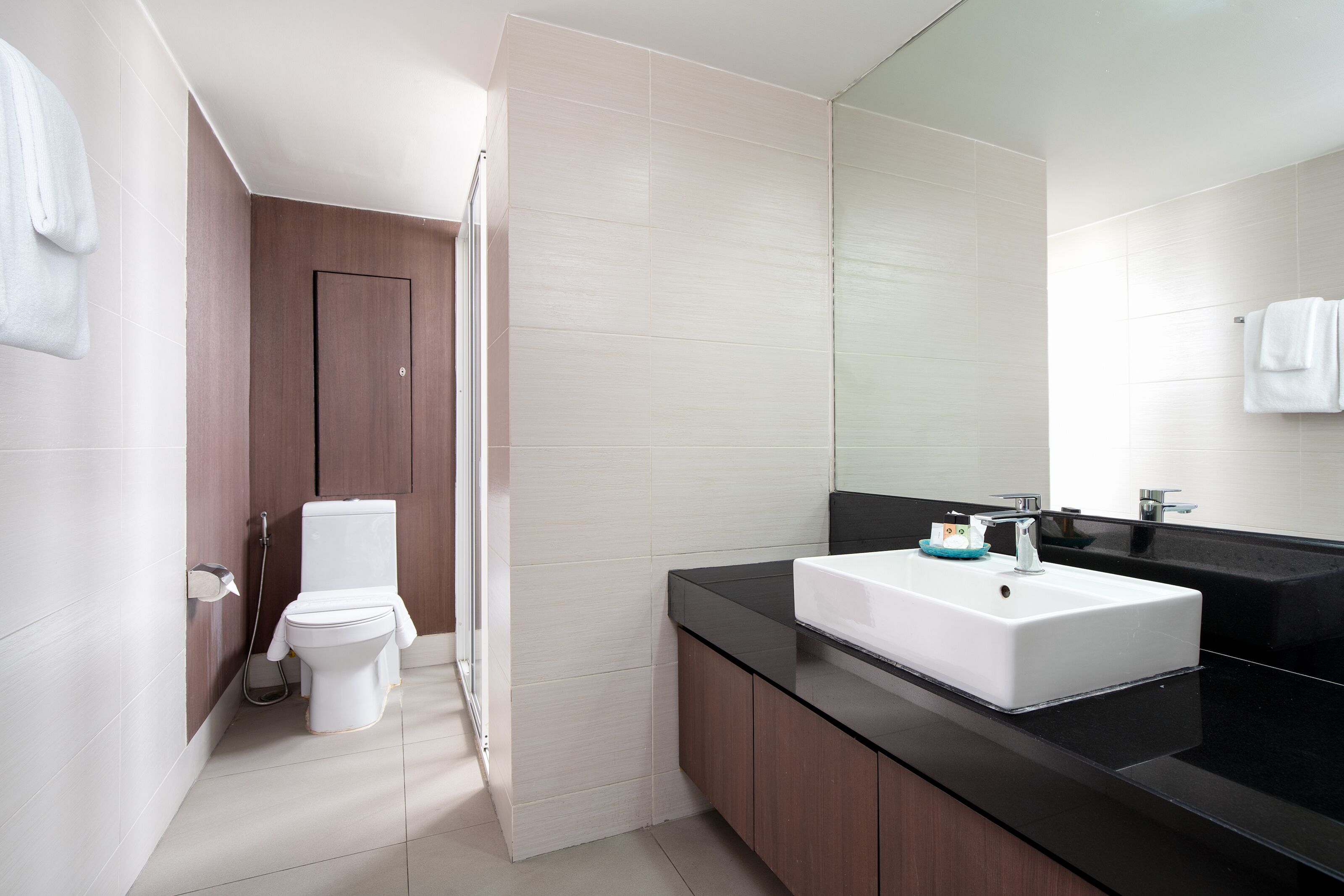 Un baño moderno con inodoro blanco, lavamanos negro y un espejo grande.