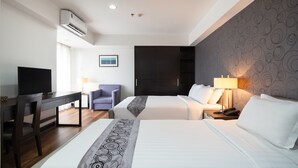 Une chambre d’hôtel avec deux lits, un bureau, une chaise, une télévision et un climatiseur fixé au mur.