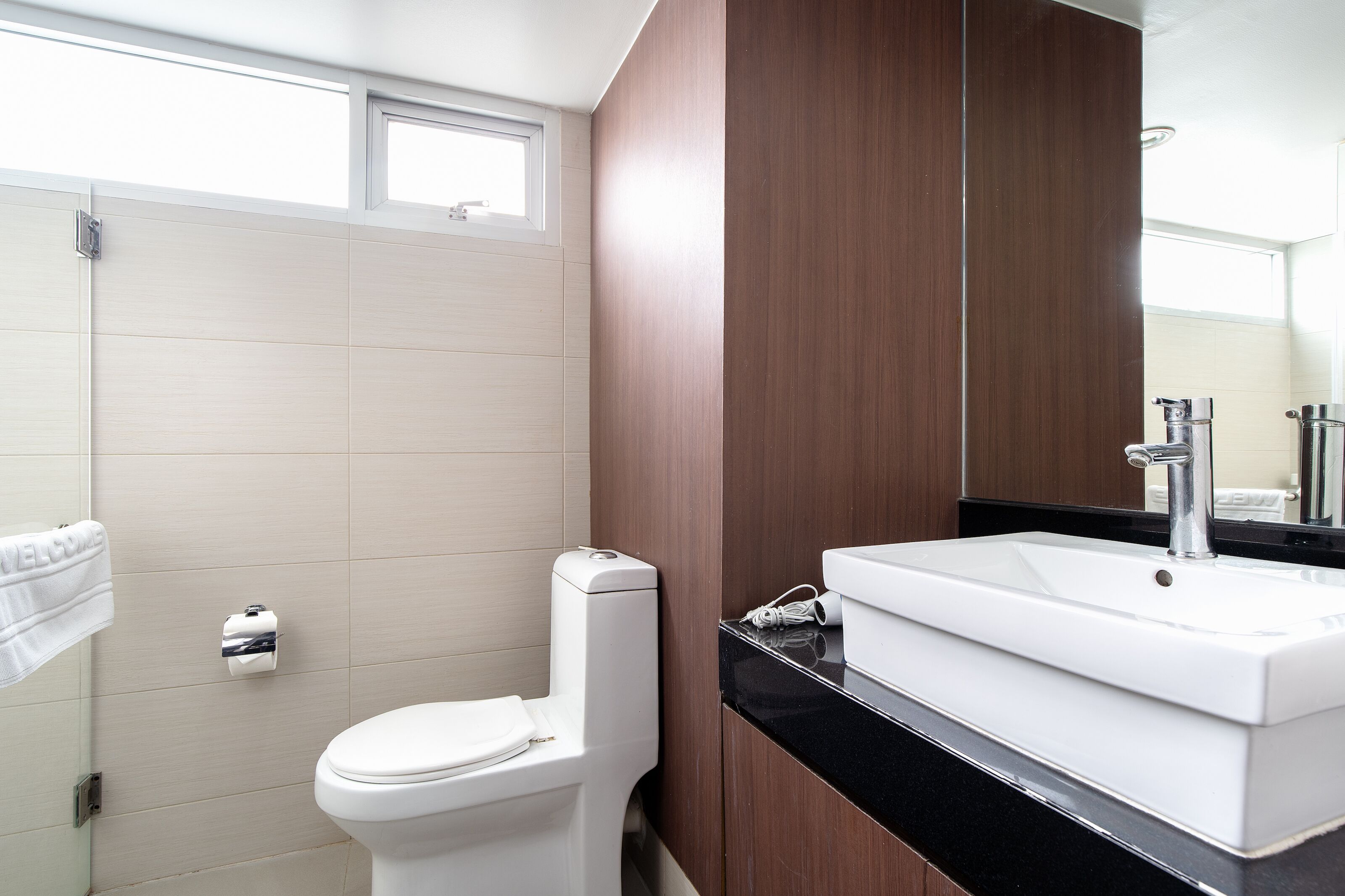 A modern bathroom with a white toilet, a sink with a black countertop, and wooden cabinetry.
