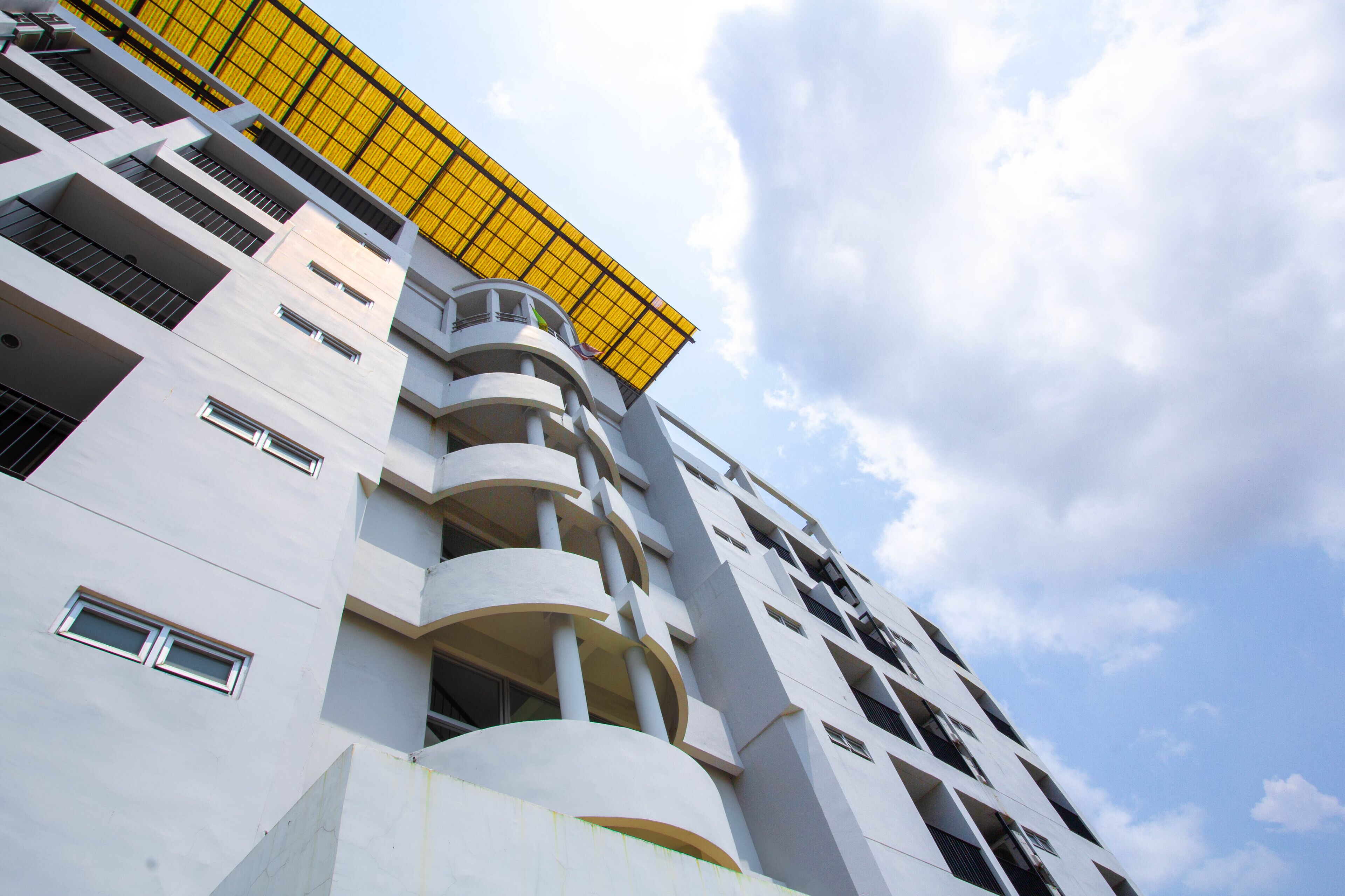 Un immeuble moderne de grande hauteur, doté de nombreux balcons et d’un toit jaune.