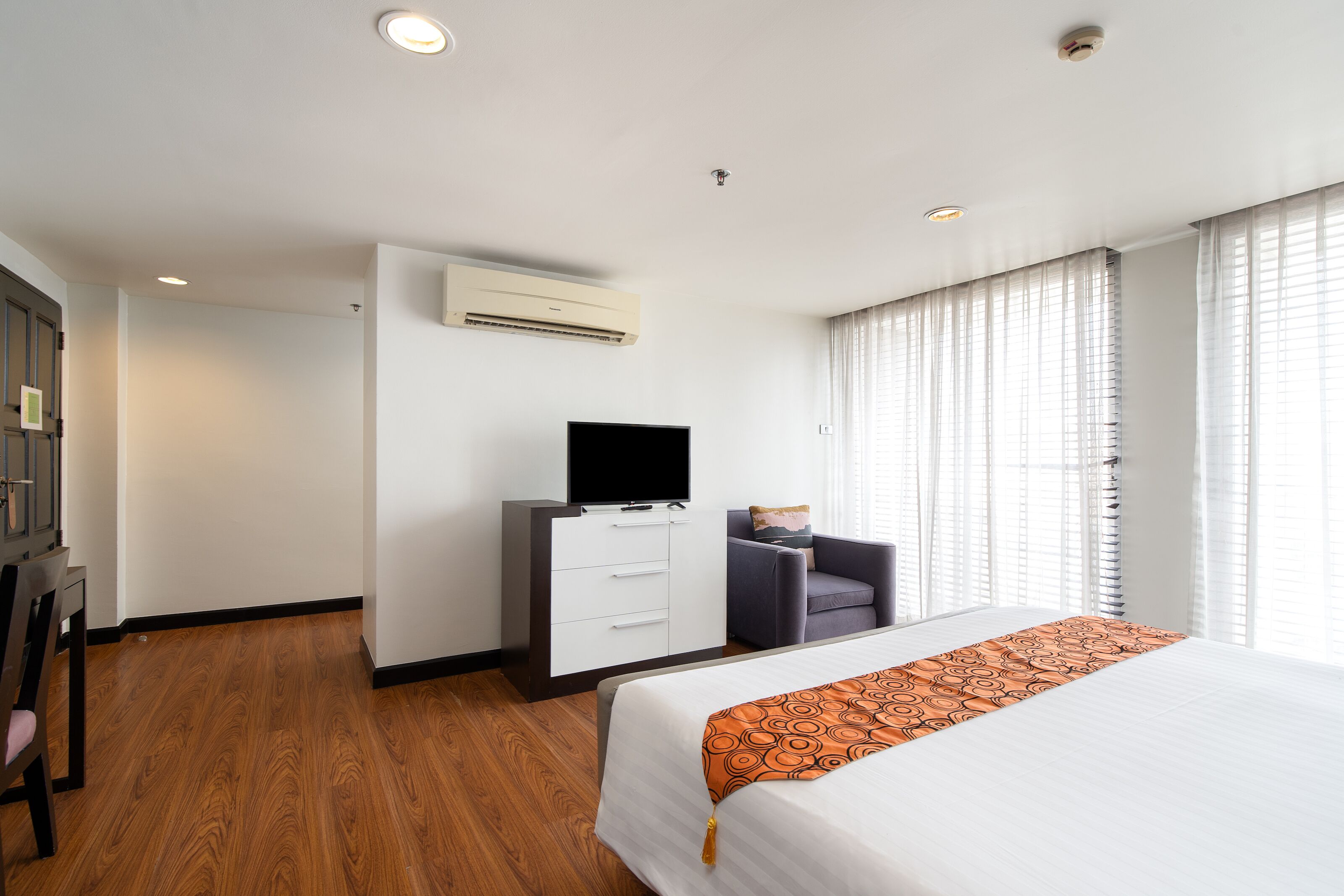 Ein Hotelzimmer mit Bett, Schreibtisch mit Flachbildfernseher, Stuhl und Fenster mit Jalousien.