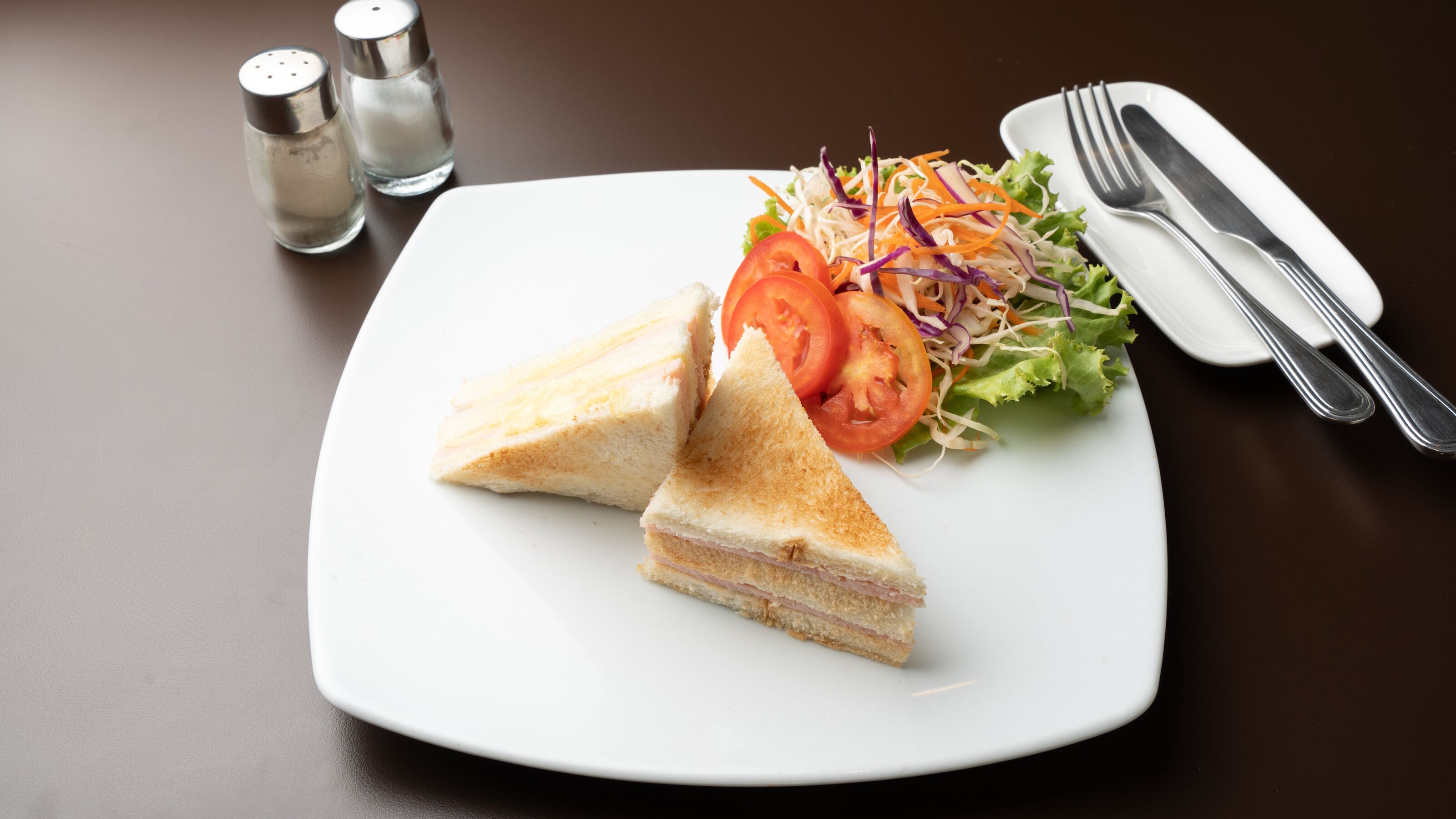 A plate with a sandwich, salad, and a fork and knife on a table.