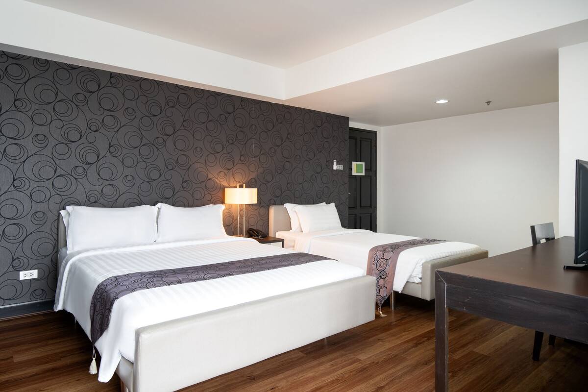 Hotellihuone, jossa on kaksi sänkyä, puulattia, tumma kuvioitu seinä ja televisio pöydällä.