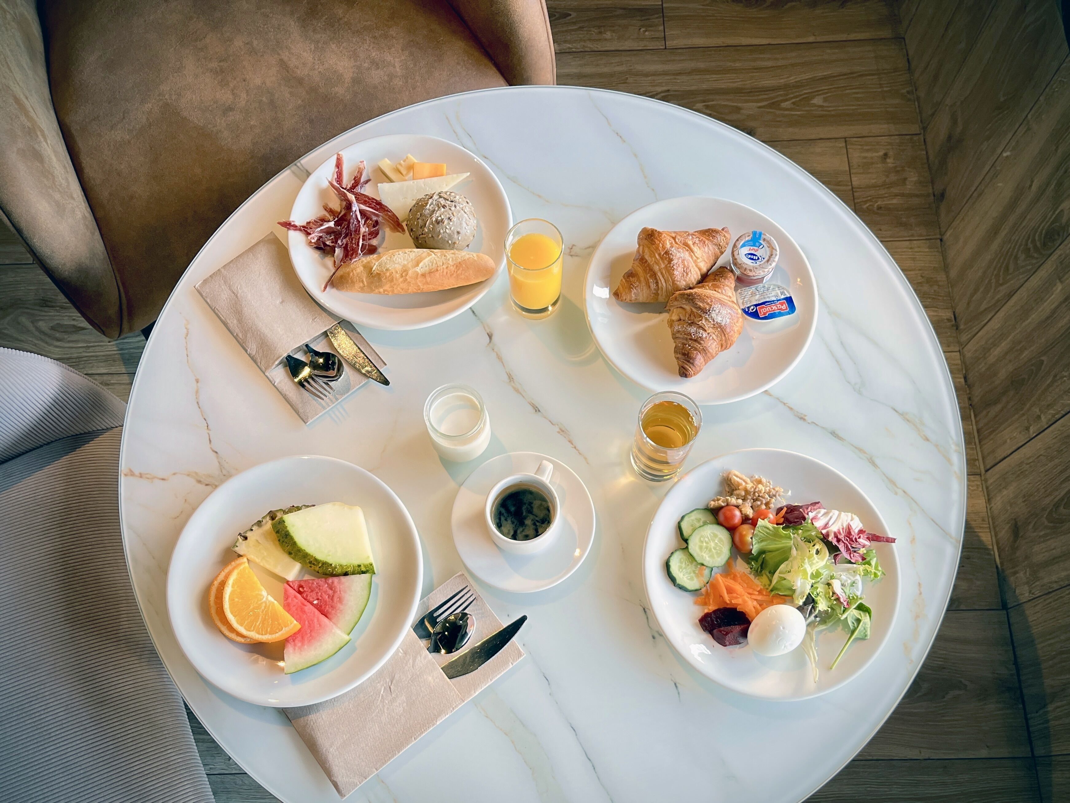 A breakfast setting with plates of food, croissants, and juice on a marble table.