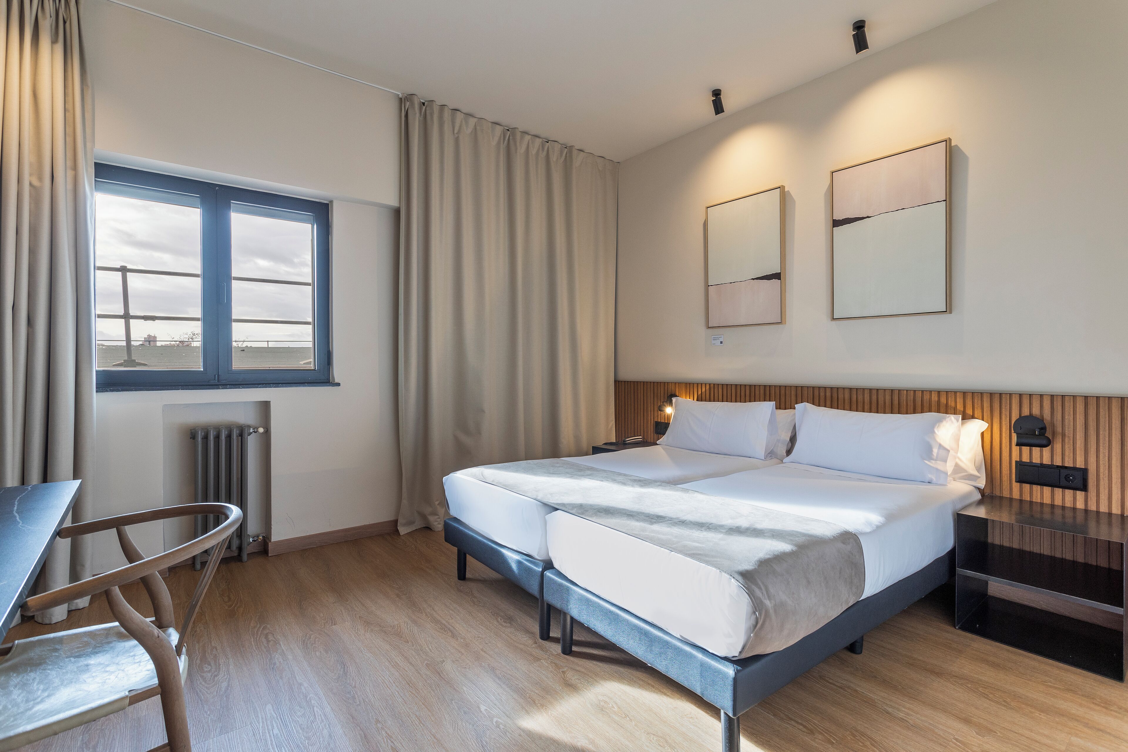 Une chambre d’hôtel avec un lit, une chaise, un bureau, une fenêtre et un radiateur.