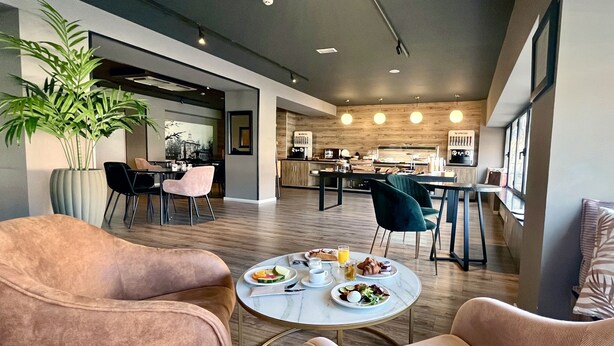 A modern dining area with round tables, plush chairs, and a large potted plant. - Hotel Acta Madfor (Madrid)