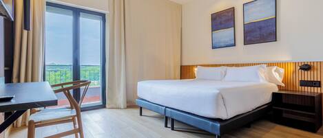 Habitación de hotel con cama, escritorio, silla, televisor y balcón con cortinas.