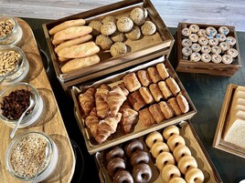 Különféle, sütőben készített péksütemények – például kenyerek, croissant-ok és fánkok – fa tálcákon vannak kiállítva.