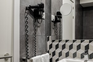 A bathroom with a hairdryer mounted on the wall, a towel rack, a mirror, and a sink with a bottle of hand soap.