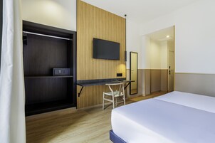 Ein Hotelzimmer mit Bett, Schreibtisch mit Stuhl, einem an der Wand befestigten Fernseher und einem Kleiderschrank.