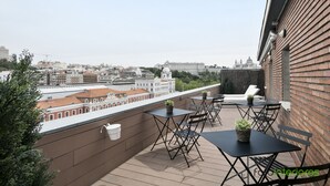 A rooftop terrace with tables and chairs, a potted plant, and a view of city buildings. - Hotel Acta Madfor (Madrid)